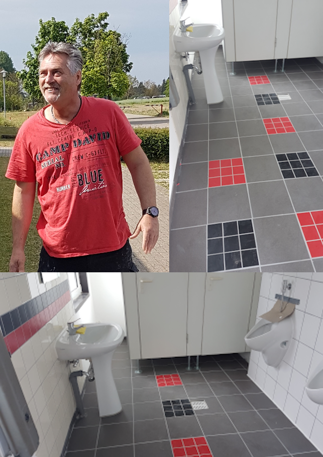Mann in rotem Shirt steht in einem Badezimmer mit Toilette und Waschbecken.