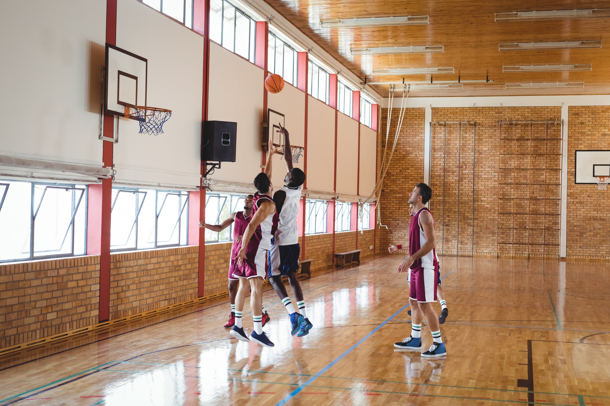 Zwei Basketballspieler in einer Halle, die sich auf das Spiel konzentrieren, mit Korb und Zuschauer im Hintergrund.