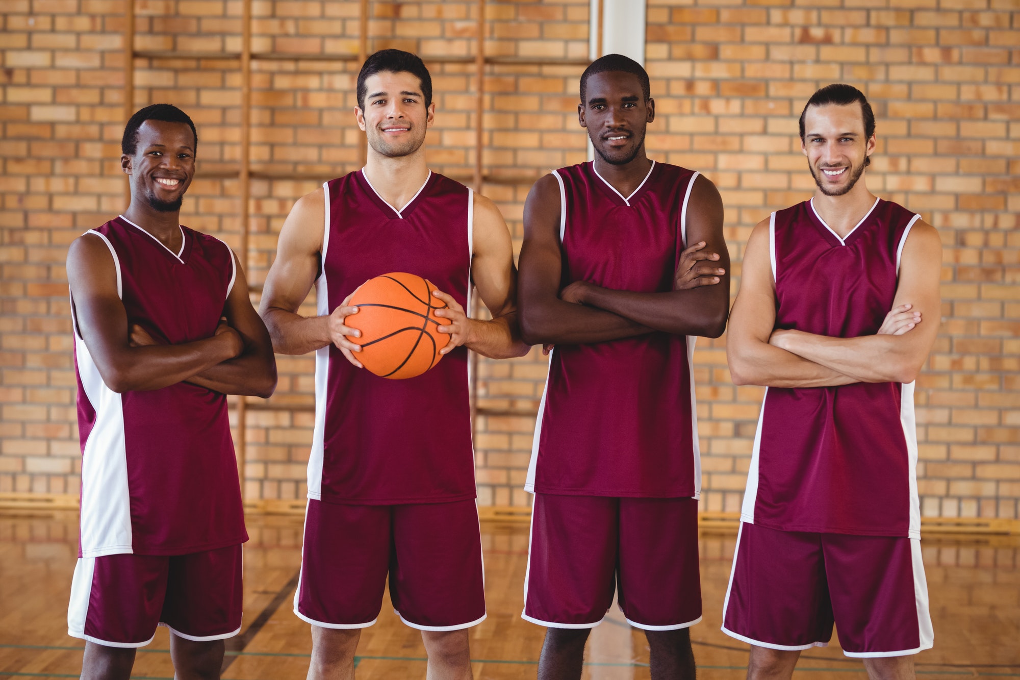 Vier Männer in burgunderfarbenen Basketballoutfits stehen in einem Gymnastikraum.
